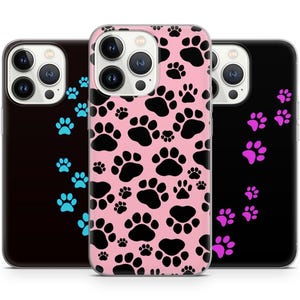 Op de afbeelding: Drie telefoonhoesjes met verschillende poot afdruk ontwerpen. Het hoesje links heeft blauwe poot afdrukken op een zwarte achtergrond. Het hoesje in het midden heeft roze poot afdrukken op een witte achtergrond. Het hoesje rechts heeft paarse poot afdrukken op een zwarte achtergrond.