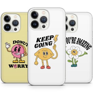 Könnte beinhalten: Drei iPhone-Hüllen mit unterschiedlichen Designs. Die erste Hülle ist gelb mit einem rosafarbenen Donut-Charakter und dem Text "Keine Sorge". Die zweite Hülle ist weiß mit einem gelben Zitronen-Charakter und dem Text "Weitermachen". Die dritte Hülle ist weiß mit einem weißen Blumen-Charakter und dem Text "Du bist toll".