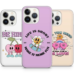 May include: Three phone cases with different designs. The first case is white with a pink cherry design and the text "Be Kind". The second case is purple with a yellow flower design and the text "Life is Short, Est 2023, Make it More Fun". The third case is beige with a rainbow and two pink hearts design and the text "All You Need is Love!".