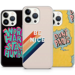 May include: Three iPhone cases with different designs. The first case is black with the text "Work Hard Stay Humble" in pink and blue. The second case is beige with a rainbow stripe design and the text "Be Nice" in black. The third case is yellow with a blue speech bubble that says "Don't Panic" in pink.