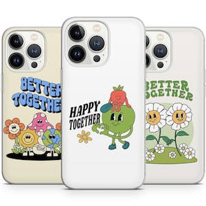 Könnte beinhalten: Drei iPhone-Hüllen mit verschiedenen Designs. Die erste Hülle hat einen hellgelben Hintergrund mit einer grünen, blauen und gelben Cartoon-Blume, einem Pilz, einer Sonne und einer Erde. Der Text "Better Together" ist in einer Retro-Schriftart. Die zweite Hülle hat einen weißen Hintergrund mit einer grünen Cartoon-Figur, die einen grünen Apfel mit einer roten Cartoon-Figur darauf hält. Der Text "Happy Together" ist in einer Retro-Schriftart. Die dritte Hülle hat einen weißen Hintergrund mit zwei weißen Cartoon-Gänseblümchen mit gelben Zentren. Der Text "Better Together" ist in einer Retro-Schriftart.