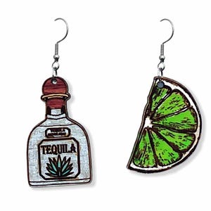 Op de afbeelding: Een paar houten oorbellen met een tequilafles en een limoenwig. De tequilafles is wit met een rode dop en het woord "TEQUILA" gedrukt op het etiket. De limoenwig is groen en heeft een bruine steel.