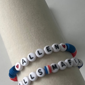 May include: Two beaded bracelets with the names "ALLEN" and "LLSMAFIA" spelled out in black letters on white beads. The bracelets are made with blue, red, and white beads. Each bracelet has a small red heart charm.