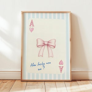 Puede incluir: Una impresión enmarcada de una carta de juego con un lazo rosa en ella. La carta es un as de corazones y el texto en la carta dice "How lucky are we?"