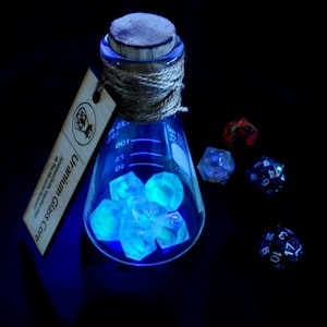 May include: A glowing blue glass flask containing luminous, irregularly shaped stones, labeled "Uranium Glass Core." The flask is sealed with a cork and twine. Several polyhedral dice are scattered nearby, with visible numbers.