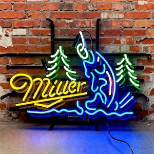 Może przedstawiać: Neonowy znak z napisem "Miller" w żółtym kursywą, z niebiesko-białym przedstawieniem ryby wyskakującej z wody. Zielone i białe neonowe drzewa flankują rybę. Znak jest zamontowany na czarnej metalowej ramie na tle ceglanej ściany.