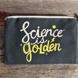 May include: A dark gray canvas pencil case with a white zipper and the words "Science is Golden" in white and yellow script. Markers and a silver tool are visible.