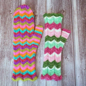 May include: Two pairs of colorful knitted fingerless gloves with a chevron pattern. One pair is pink, green, and white, and the other is pink, purple, green, and blue.