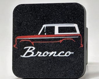 Peut inclure: Cache d'attelage carré noir avec un contour blanc d'un Ford Bronco rouge et le mot "Bronco" en lettres blanches.