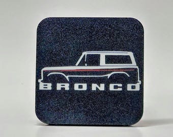 Peut inclure: Un dessous de verre carré noir avec un contour blanc d'un Ford Bronco et le mot "BRONCO" en lettres blanches.