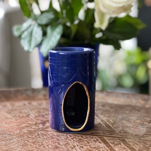 Peut inclure: Un brûleur à huile en céramique bleu avec un bord doré et une découpe au centre. Le brûleur est posé sur un plateau décoratif.