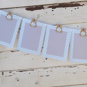 May include: A blue and white chevron patterned banner with four photo frames. Each frame has a brown teddy bear with a number on it. The numbers are 1, 2, 3, and 4.