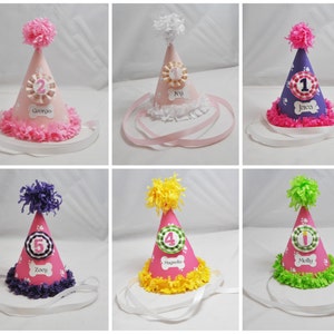 May include: Six pink and white dog party hats with different colored trims and names on each hat. The names are: Georgia, Ivy, Jawa, Zocy, Magnolia, and Molly.