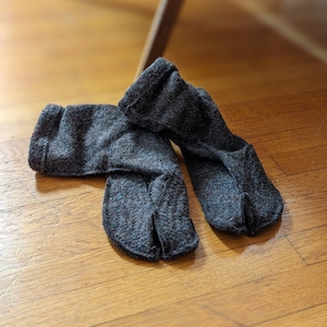 a pair of tabi split toe house slippers in medium brown wool blend on a warm oak floor