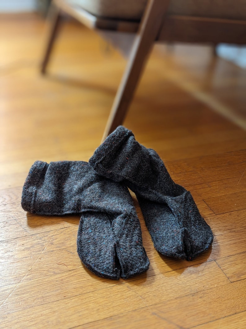 a pair of tabi split toe house slippers in medium brown wool blend on a warm oak floor