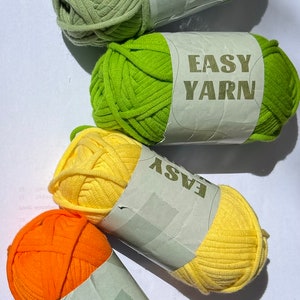 May include: Four balls of yarn in different colours: green, lime green, yellow, and orange. Each ball has a white label that says "EASY YARN".