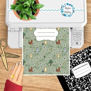 May include: A composition notebook with a green floral pattern featuring cartoon animals and the text "Composition Notebook." The notebook is printed on a printer with a plant and scissors nearby.