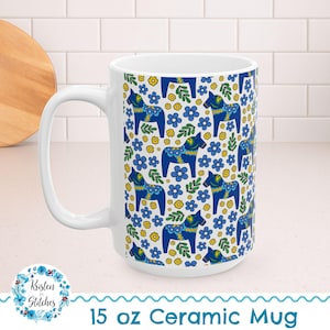 May include: White 15 oz ceramic mug featuring a repeating pattern of blue Dala horses, blue flowers, and yellow floral accents. The mug has a large handle and the text "15 oz Ceramic Mug" is printed on the bottom.