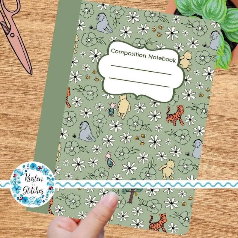 May include: A composition notebook with a green cover featuring a floral pattern and cartoon characters. The notebook has the words "Composition Notebook" on the front. The design includes Winnie the Pooh, Piglet, Tigger, and Eeyore.