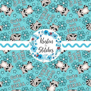 May include: A repeating pattern on a light blue background featuring cartoon raccoons, blue flowers, and stars. The phrase "Cute but Feral" is repeated throughout the design. A circular logo with the text "Kristen in Stitches" is also present.