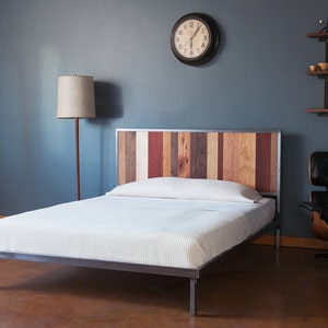 May include: A metal bed frame with a wooden headboard made of reclaimed wood planks in various shades of brown, red, and white. The bed frame has a white mattress and is sitting on a brown floor.