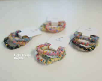 May include: Three sets of colorful fabric hair ties, each set containing three ties. The ties are made of a soft, textured fabric with a variety of colors and patterns. The sets are packaged on white cards with the text "Little Forest Breeze".