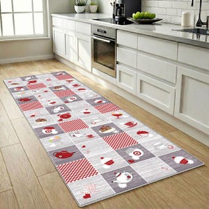 Könnte beinhalten: Ein rechteckiger Küchenteppich mit einem sich wiederholenden Muster aus roten und grauen Quadraten. Jedes Quadrat zeigt Illustrationen von Teekannen, Teetassen, Kuchen und Cupcakes. Der Teppich liegt auf einem Holzboden vor einer weißen Küche.