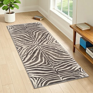 May include: A rectangular rug with a zebra stripe pattern in shades of brown and cream. The rug is placed on a light-colored wooden floor, with a plant and a small wooden table visible in the background. The rug's design is symmetrical.
