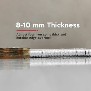 May include: Close-up of a white rug with a black edge. The rug is 8-10 mm thick, almost four iron coins thick. The text "8-10 mm Thickness" is above the rug. The text "Almost four iron coins thick and durable edge overlock" is below the rug.