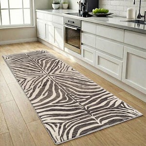 May include: A rectangular zebra-print rug in a kitchen setting. The rug features a pattern of black and cream-colored stripes, creating a bold, animal-inspired design. The rug is placed on a light-colored wooden floor, adding a touch of style to the kitchen.