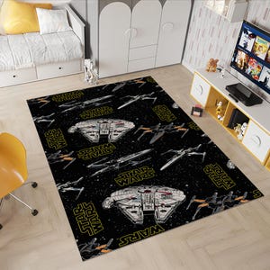 Puede incluir: Alfombra rectangular negra con temática de Star Wars, con el Halcón Milenario, cazas X-wing y el logotipo de Star Wars en amarillo. La alfombra tiene un fondo espacial y es adecuada para un dormitorio infantil o sala de juegos.