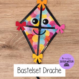 Könnte beinhalten: Ein rautenförmiger Drachen mit schwarzem Rahmen und bunten, transparenten Papierkreisen. Er hat ein lächelndes Gesicht, einen schwarzen Schwanz und vier Schleifen in Orange, Rot, Pink und Gelb. Text: "Bastelset Drache" und "Mir reicht's ICH GEH BASTELN".