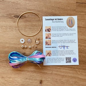 May include: A craft kit for making sun catchers, featuring a gold metal ring, beads, ribbons in blue, pink, and purple, and instructions. The kit includes a variety of components for creating decorative sun catchers.