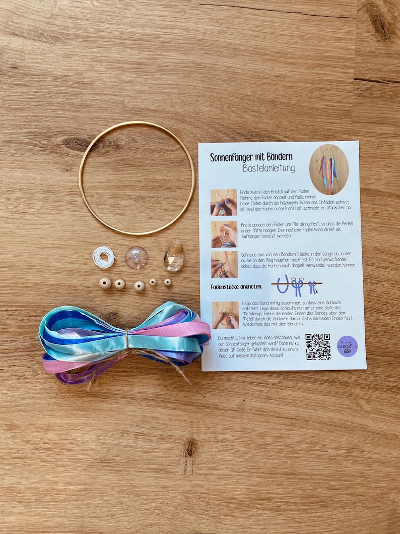 May include: A craft kit for making sun catchers, featuring a gold metal ring, beads, ribbons in blue, pink, and purple, and instructions. The kit includes a variety of components for creating decorative sun catchers.