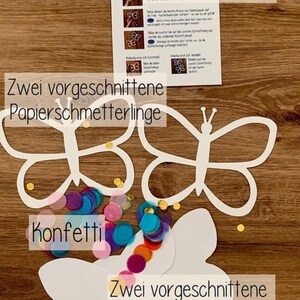 May include: A craft kit for making butterfly window decorations. The kit includes two pre-cut paper butterflies, confetti, and two pre-cut adhesive sheets. The instructions are in German.