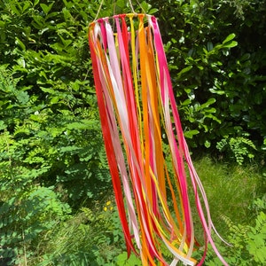 May include: A colourful wind chime with ribbons in shades of pink, orange, yellow, and white hanging from a circular frame.