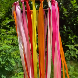 May include: A colourful mobile with ribbons in shades of pink, yellow, orange, and red hanging from a circular metal frame.