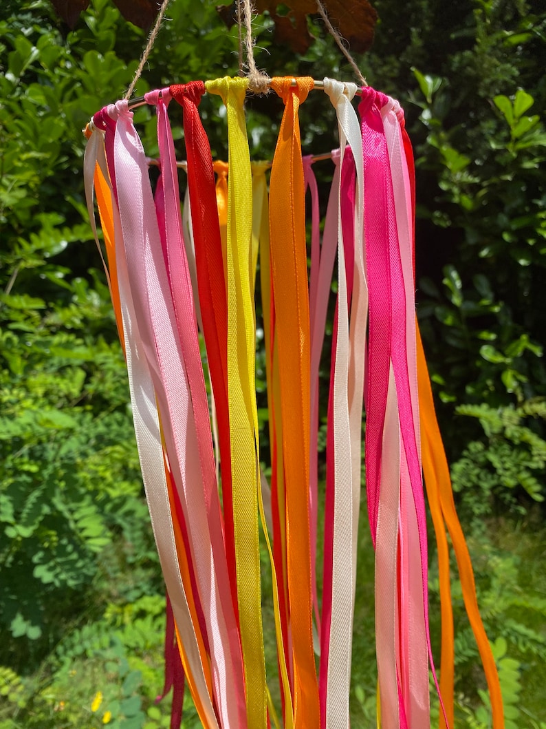 May include: A colourful mobile with ribbons in shades of pink, yellow, orange, and red hanging from a circular metal frame.