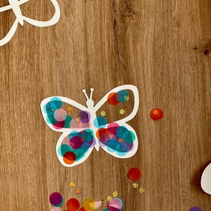May include: A white paper butterfly cutout with colourful tissue paper circles glued on. The butterfly is surrounded by more tissue paper circles in various colours, including red, blue, green, purple, and gold.
