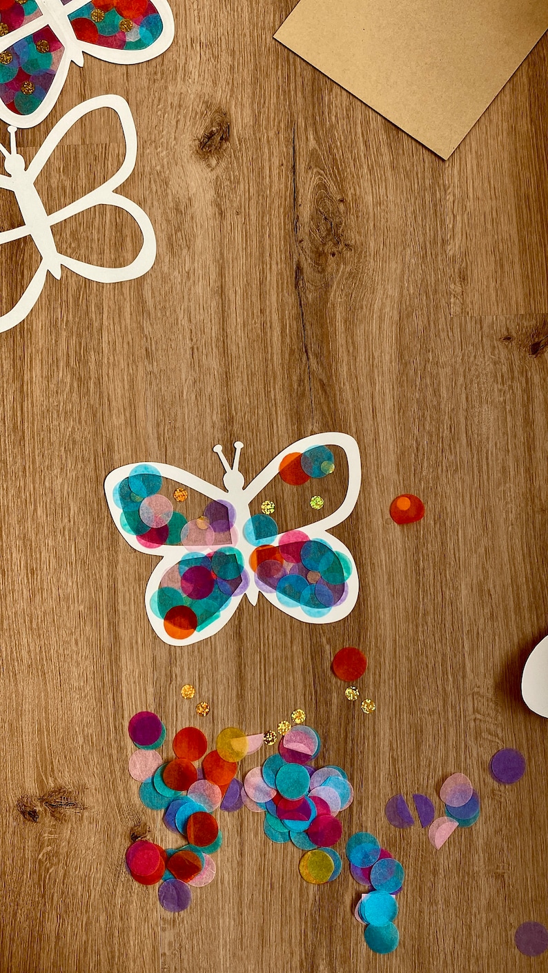 May include: A white paper butterfly cutout with colourful tissue paper circles glued on. The butterfly is surrounded by more tissue paper circles in various colours, including red, blue, green, purple, and gold.