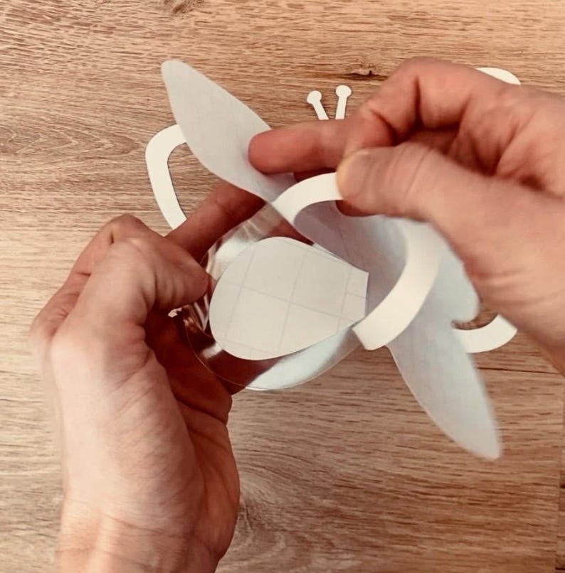 May include: A white paper butterfly craft with a cut-out design. The butterfly is being folded in half to create a three-dimensional shape.