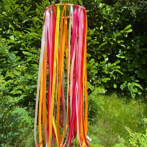 May include: A colourful mobile with ribbons in pink, yellow, and orange hanging from a circular frame. The mobile is suspended from a string.
