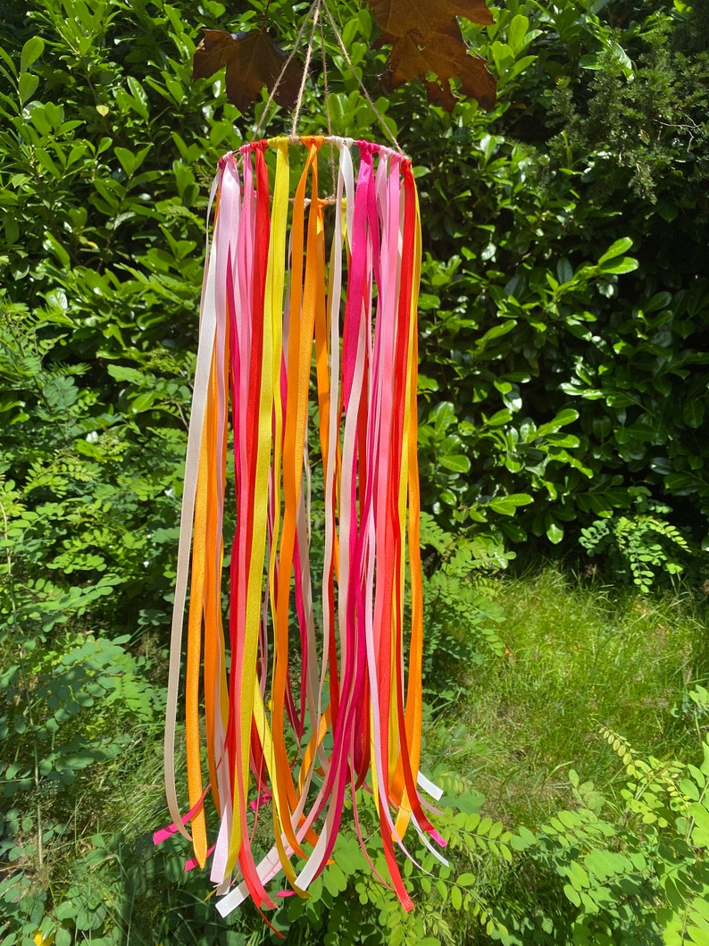 May include: A colourful mobile with ribbons in pink, yellow, and orange hanging from a circular frame. The mobile is suspended from a string.