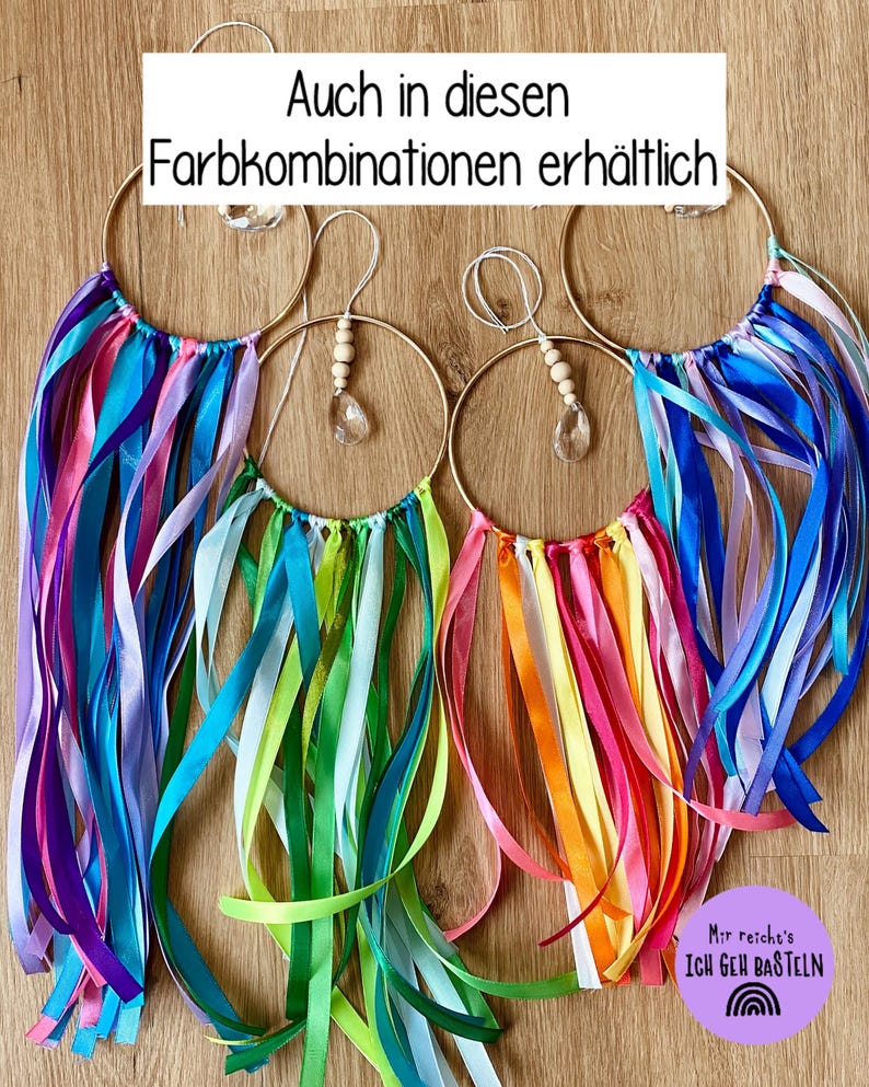 May include: Four decorative hoop ornaments with colorful ribbons in shades of blue, pink, green, and orange. Each hoop has a gold-colored ring and a crystal or wooden bead accent. The text "Auch in diesen Farbkombinationen erh&auml;ltlich" is visible.