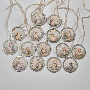 May include: A collection of round, silver-rimmed ornaments with illustrations of bunnies in a field of flowers. Each ornament is attached to a natural twine string. The bunnies are depicted in various poses and colors, set against a soft, pastel background.