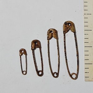 May include: Four rusty safety pins of different sizes, arranged in order of size, with the largest pin measuring approximately 2 inches in length.