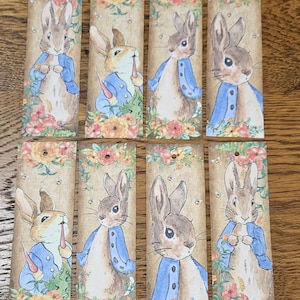 May include: Set of eight bookmarks featuring a cartoon rabbit wearing a blue jacket and holding a carrot. The bookmarks have a brown background with floral designs and a white border.