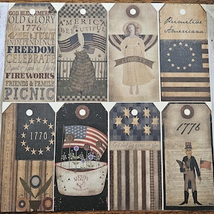 May include: Nine vintage-style paper tags with patriotic themes. The tags feature images of an angel, a beehive, a flag, a farmer's market, and a man in a red, white, and blue outfit. The tags also include text such as "God Bless America", "Old Glory", "America Beautiful", "Liberty", "Primitive Americana", "1776", "Red White Blue", "God Shed His Grace on Thee", and "We the People".