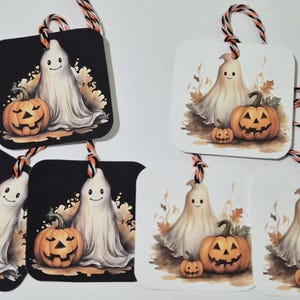 May include: Five square gift tags featuring a white ghost and orange jack-o'-lantern pumpkins. Three tags have a black background and two have a white background. Each tag is attached to a piece of orange, black, and white twisted twine.