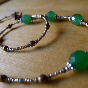 May include: A necklace with faceted green beads and smaller silver and bronze-toned beads. The beads are strung on a thin wire, creating a flowing design. The necklace has a delicate appearance. The beads have a subtle sparkle, adding a touch of elegance.